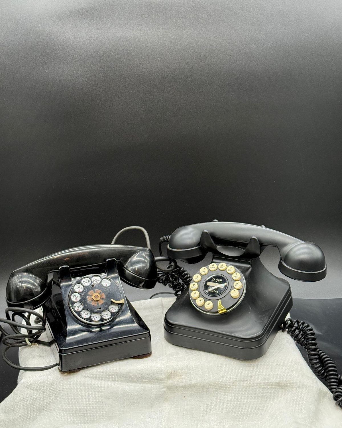 Two black vintage telephones side by side, a 1945 Bell System rotary dial phone on the left and a retro 1950s-style push-button phone on the right.