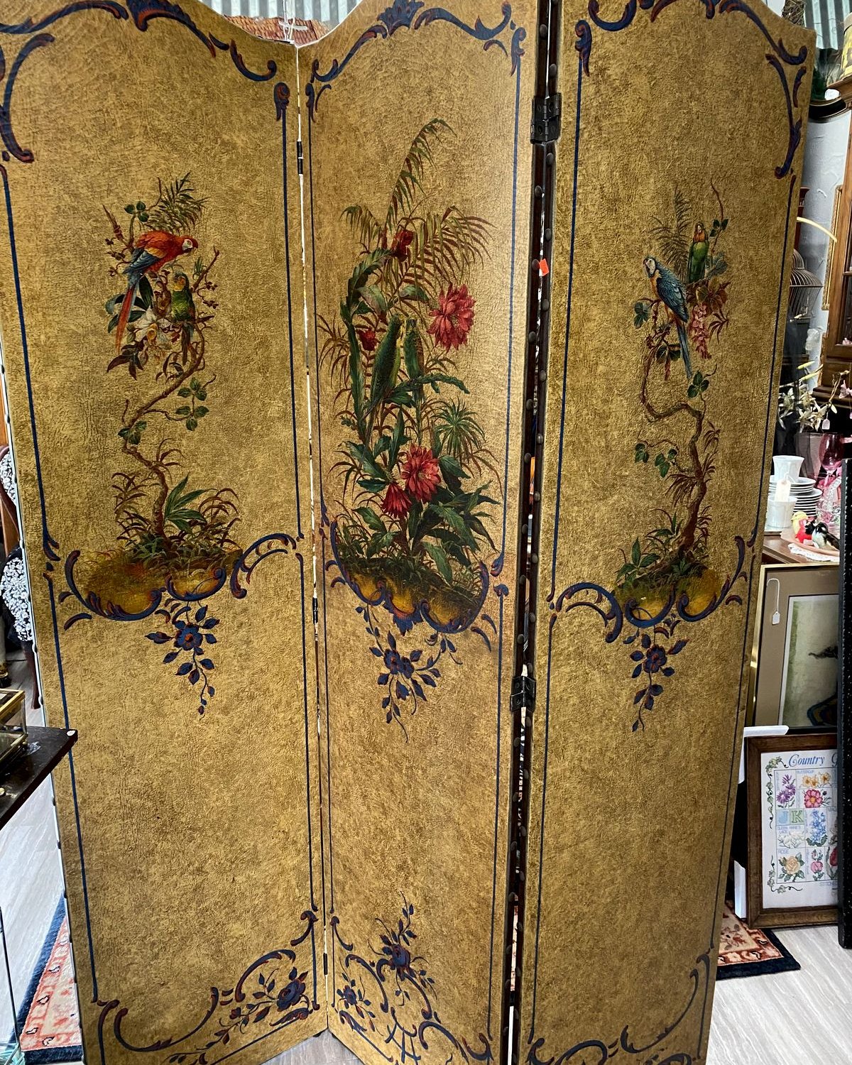 Three-panel folding screen with gold background, hand-painted tropical florals, ferns, and parrots, with classical urns at the base of each panel.