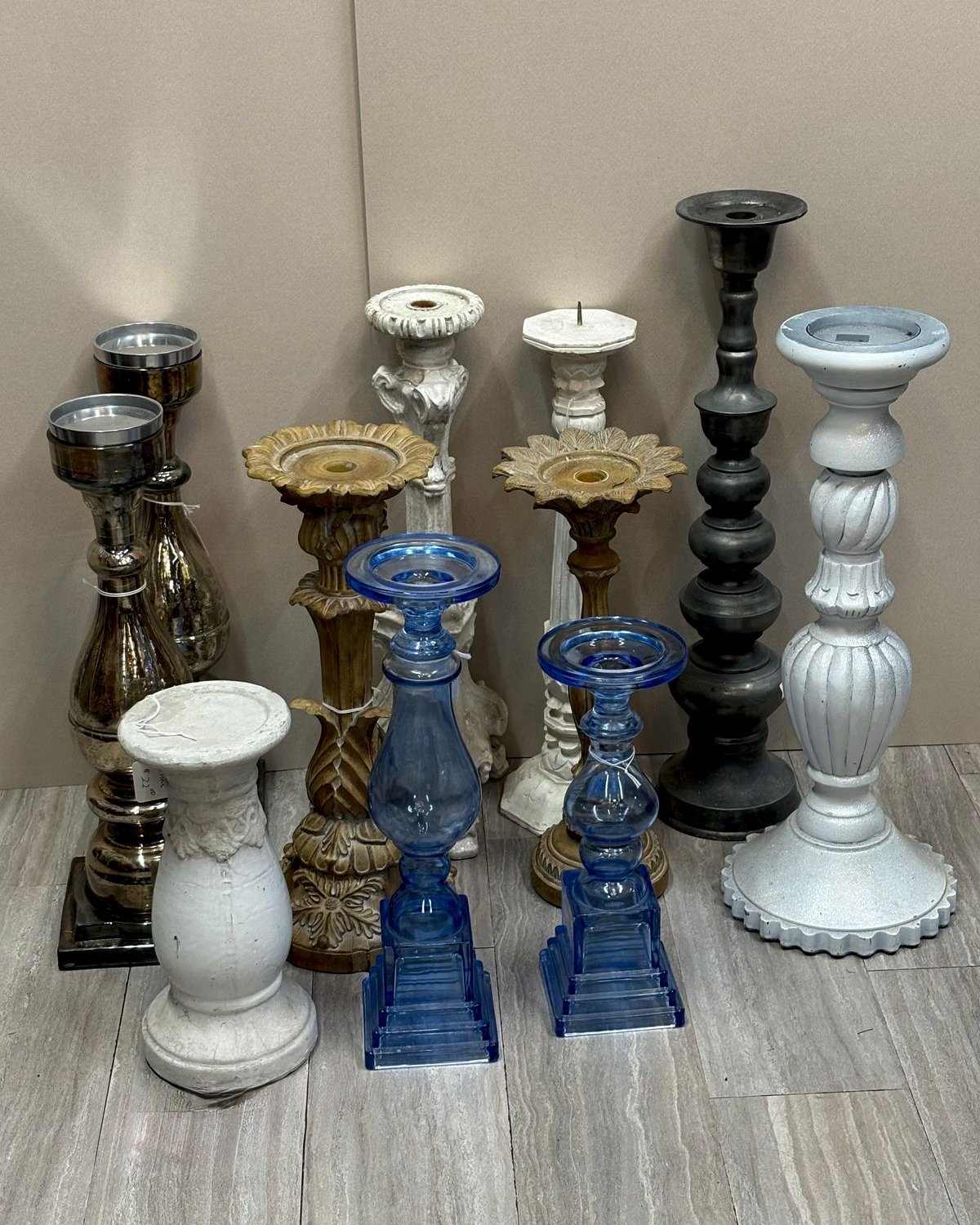 A grouping of antique and vintage candlesticks in varying heights including mercury silver glass, cobalt blue pressed glass, gilded sunflower columns, white turned-wood pillars, and black ebonized spindles.