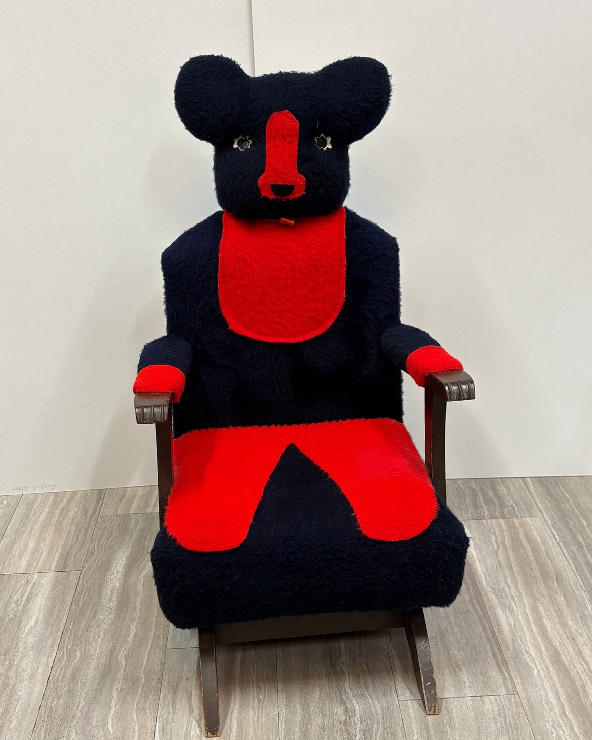 A 1960s child's rocking chair upholstered as a navy blue teddy bear with red accents, rounded ears, a red snout, a bib, and wooden rocker arms.