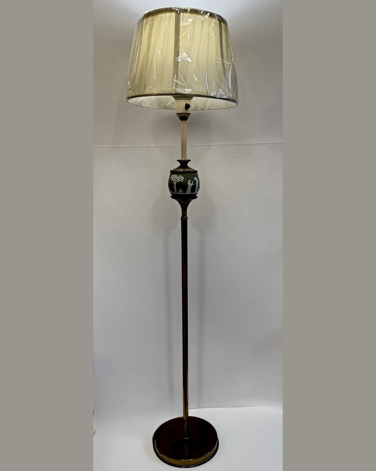 A fifty-two inch vintage brass floor lamp with a slender fluted column and round stepped base, set with a sage green jasperware ball at mid-column decorated with white neoclassical figures in relief, topped with a cream pleated shade.