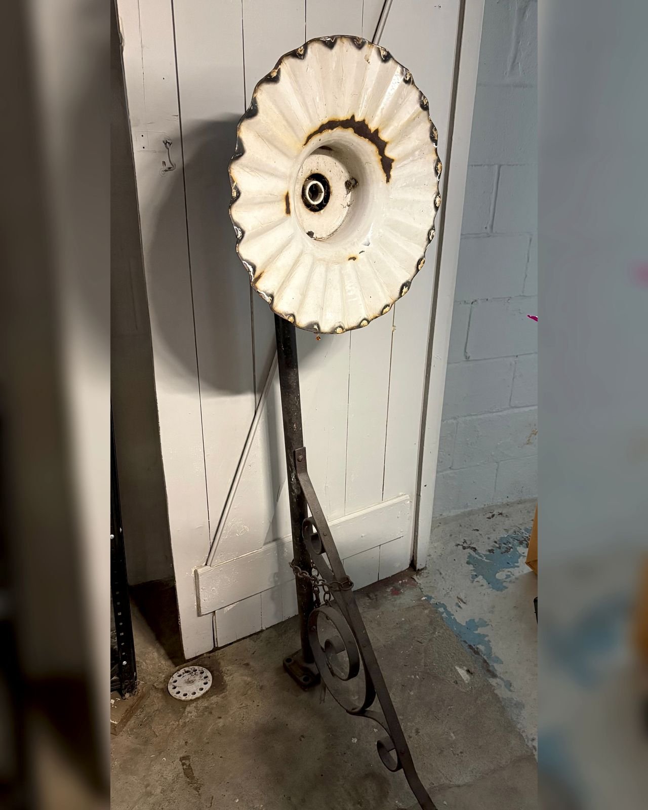 Vintage white porcelain enamel radial wave light shade with a scalloped rim, mounted on a dark iron pole with a scrolled wrought iron bracket and chain.