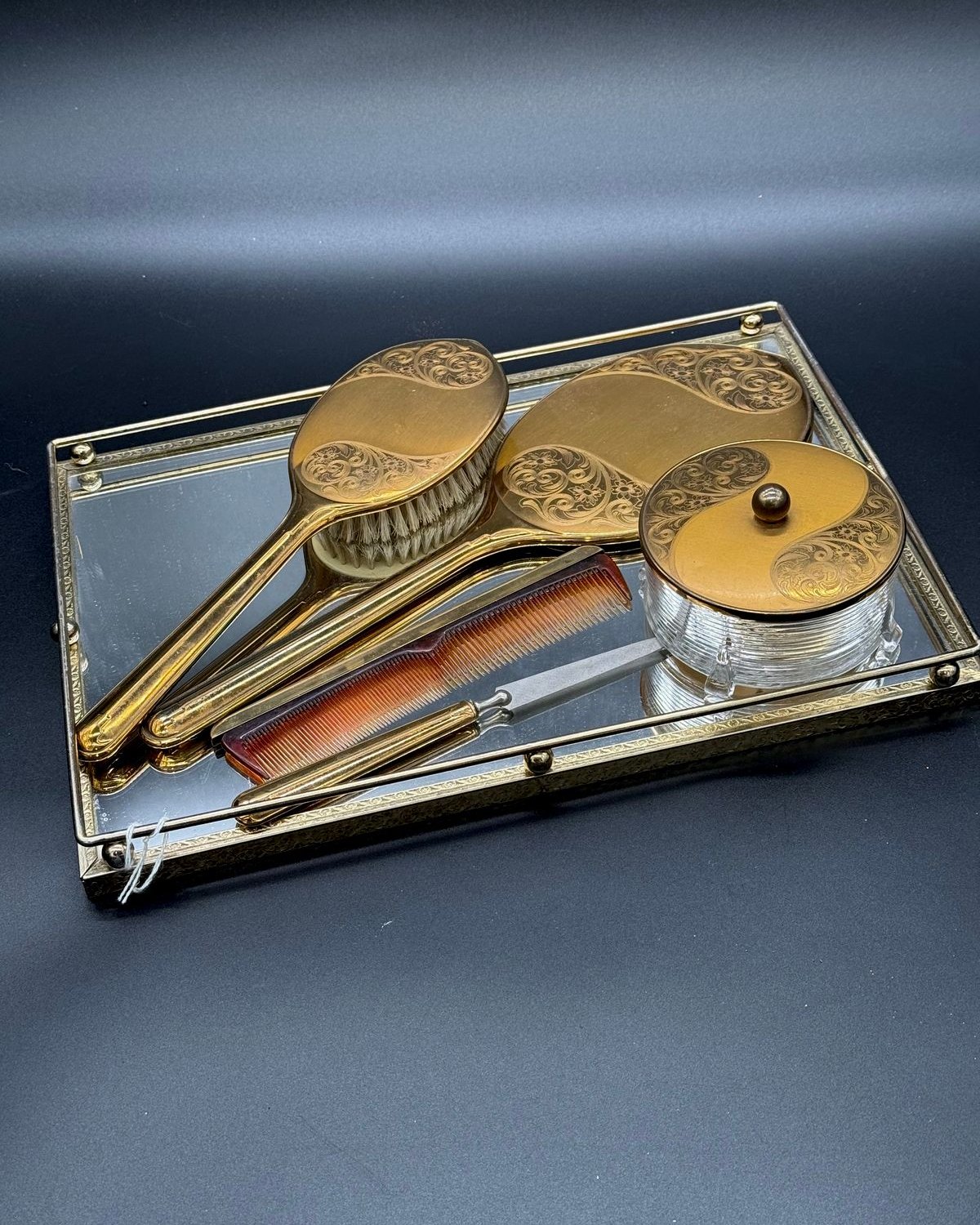 Vintage five-piece gold vanity dresser set with ornate scrollwork displayed on a mirrored gold tray
